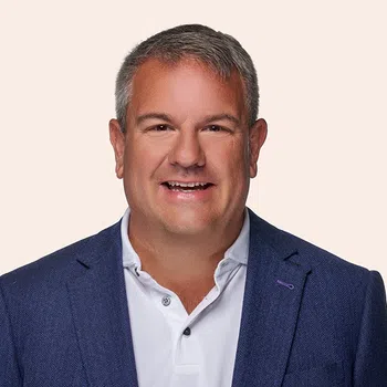 Smiling middle-aged man with gray hair wearing a blue blazer and white polo shirt on light background