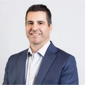 Professional man in a blue suit jacket and white shirt smiling against a plain white background